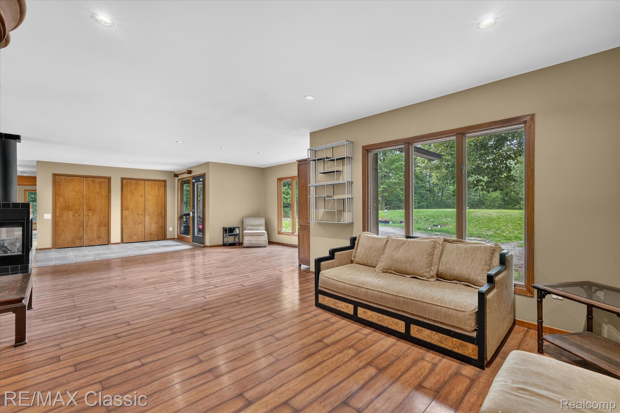 12189 Gage Road Holly, MI 48442 - Photo 7 of 69 Spacious interior featuring wood-finish flooring, a modern wood-burning stove with a tiled base, and expansive windows offering abundant natural light