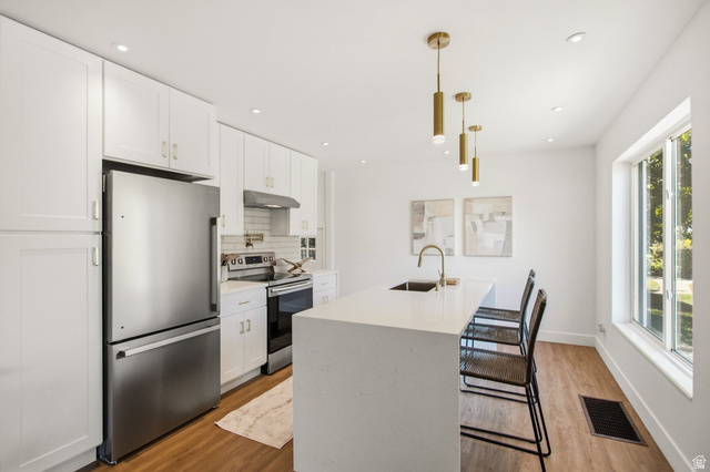 1187 East Ridgedale Circle Millcreek, UT 84106 - Photo 10 of 49 Contemporary kitchen featuring white shaker cabinetry, stainless steel appliances, a subway tile backsplash, and a large center island with integrated sink
