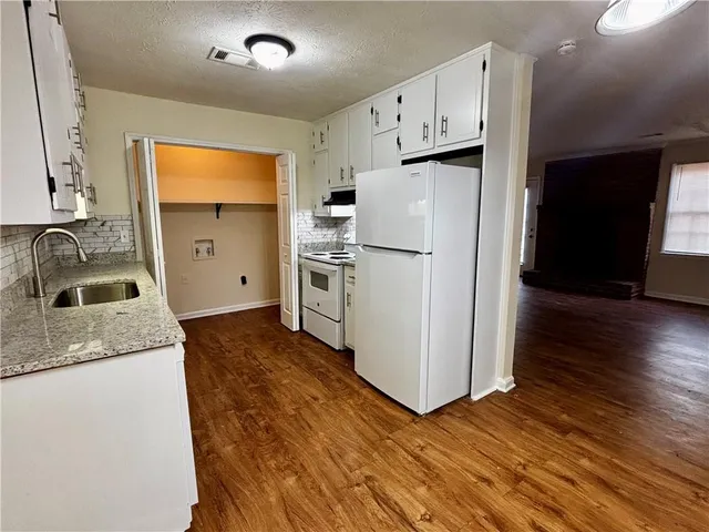 a kitchen with granite countertop a refrigerator a sink a stove and wooden floor