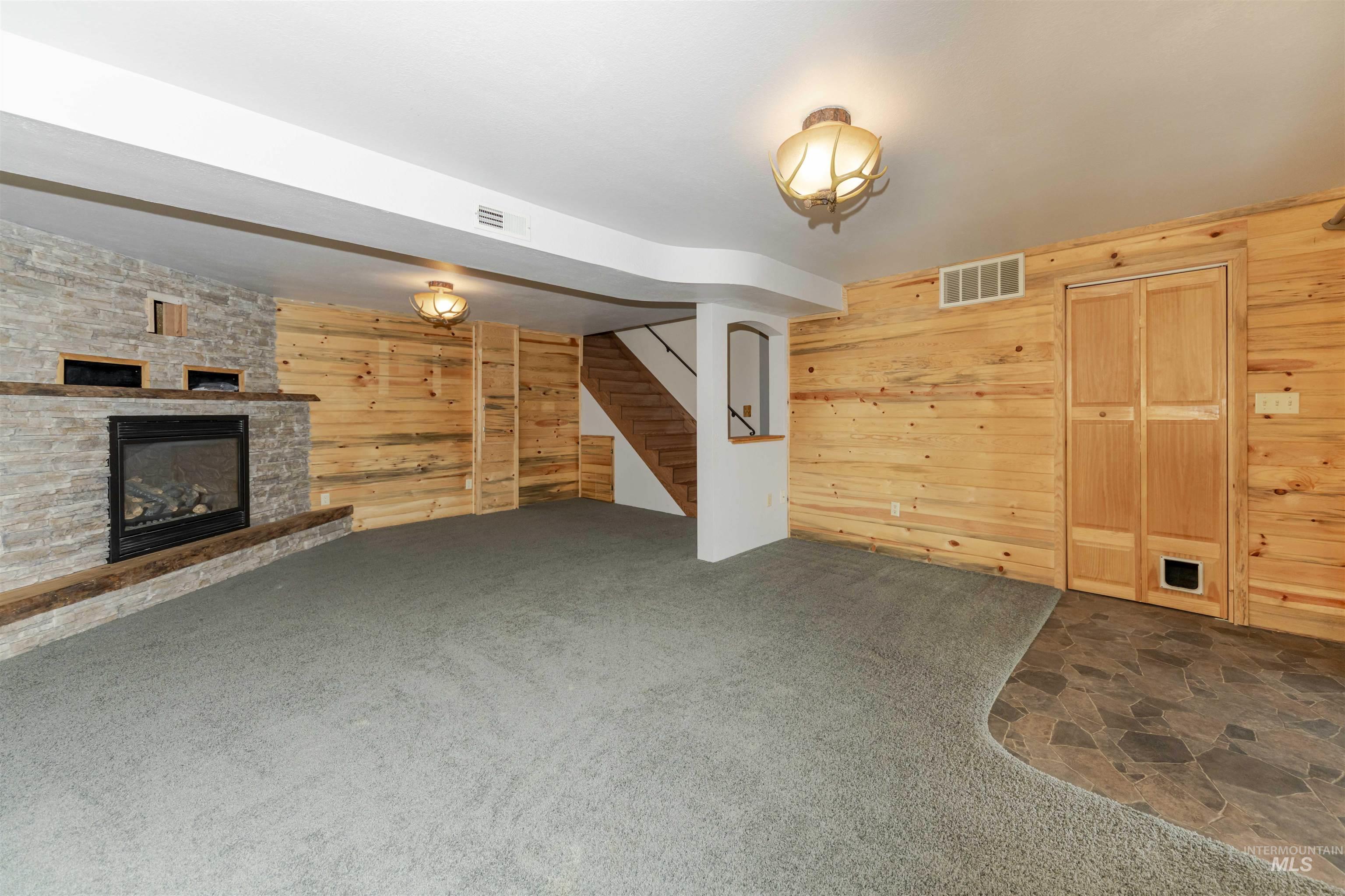1316 29th Street Lewiston, ID 83501 - Photo 21 of 31 Family room featuring wooden walls, a stone fireplace, dark carpet, and dark stone finish floors