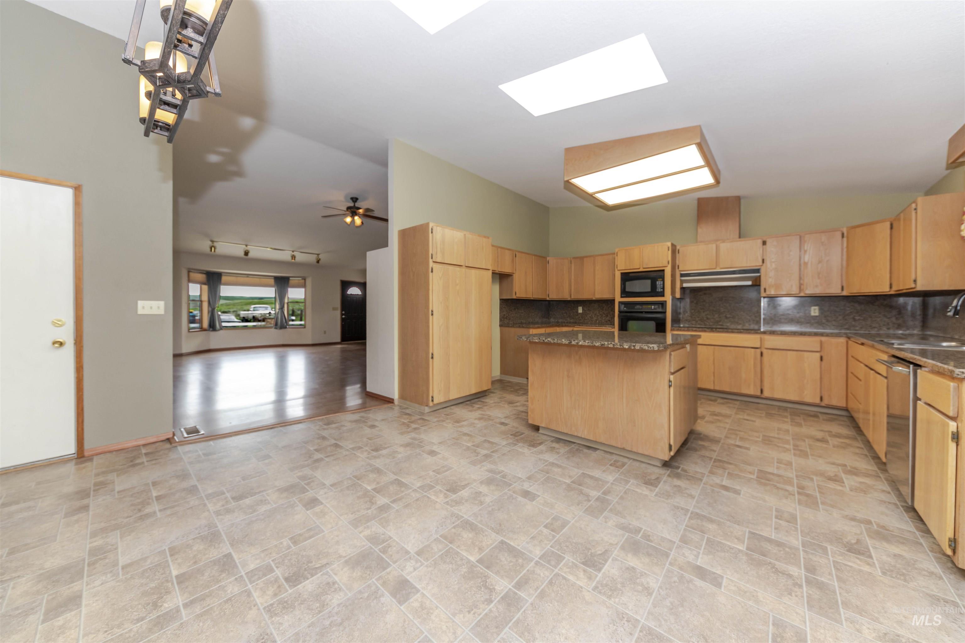 1316 29th Street Lewiston, ID 83501 - Photo 10 of 31 Kitchen with a kitchen island, stone finish floors, light wood finish cabinets, dark stone countertops, and a high ceiling