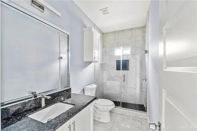 a bathroom with a granite countertop sink a toilet a mirror and shower