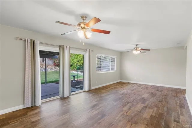 an empty room with wooden floor fan and windows