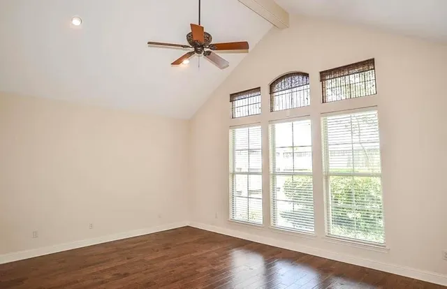 an empty room with wooden floor fan and windows