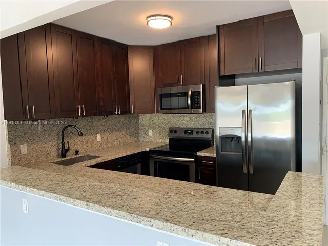 a kitchen with granite countertop wooden cabinets a refrigerator and a sink