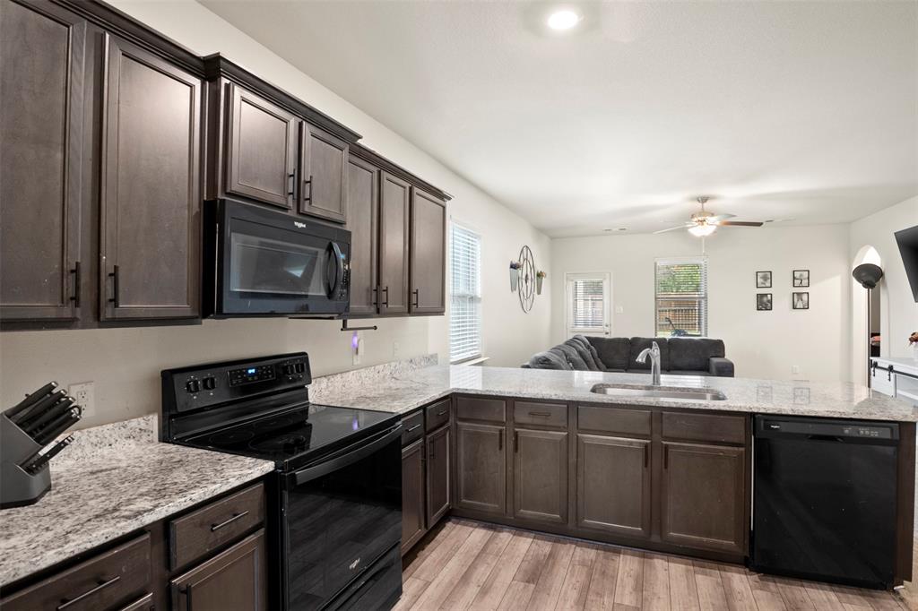 105 Patton Lane Venus, TX 76084 - Photo 26 of 29 Kitchen with dark brown cabinetry, black appliances, open floor plan, light stone countertops, and light wood finished floors
