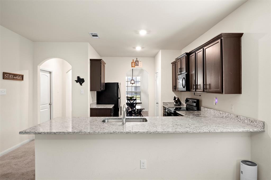 105 Patton Lane Venus, TX 76084 - Photo 11 of 29 Kitchen with dark brown cabinetry, arched walkways, a peninsula, light stone counters, and black appliances