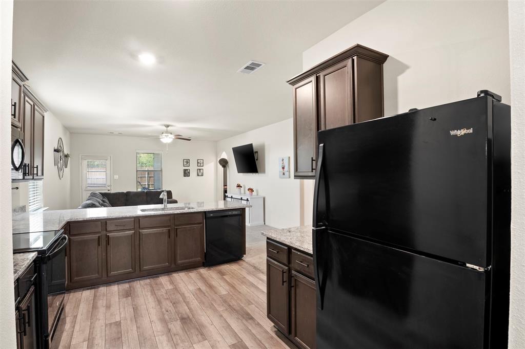 105 Patton Lane Venus, TX 76084 - Photo 27 of 29 Kitchen featuring black appliances, dark brown cabinets, open floor plan, light wood-style floors, and light stone counters