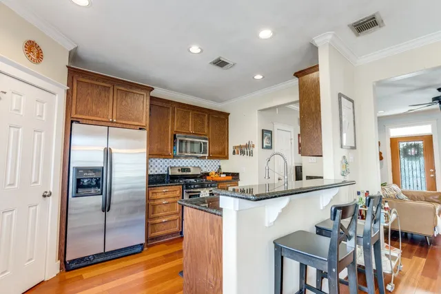 a kitchen with stainless steel appliances granite countertop a refrigerator a stove a sink and white cabinets with wooden floor