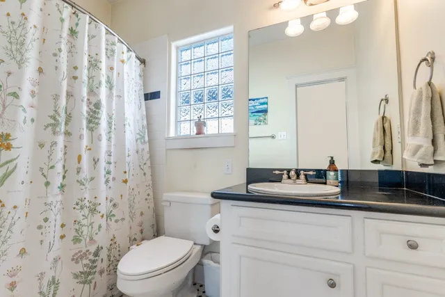 a bathroom with a granite countertop toilet a sink a mirror a window and a shower