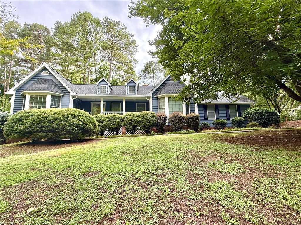 A classic Cape Cod residence with dormer windows and a welcoming front porch, nestled amidst mature trees.