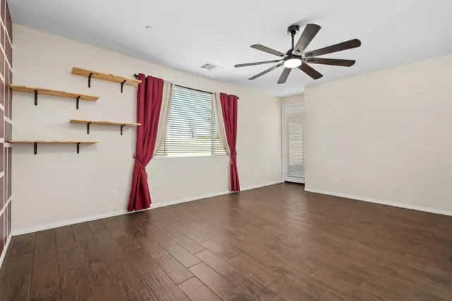 a view of an empty room with wooden floor and a ceiling fan