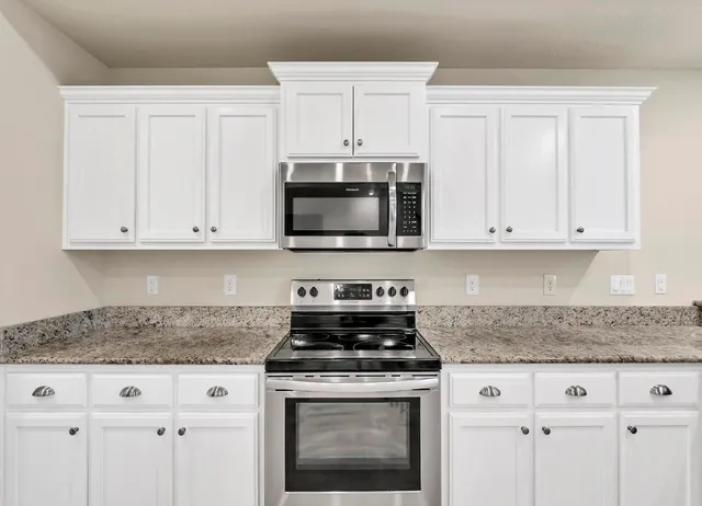 a view of an empty room with wooden floor and a kitchen