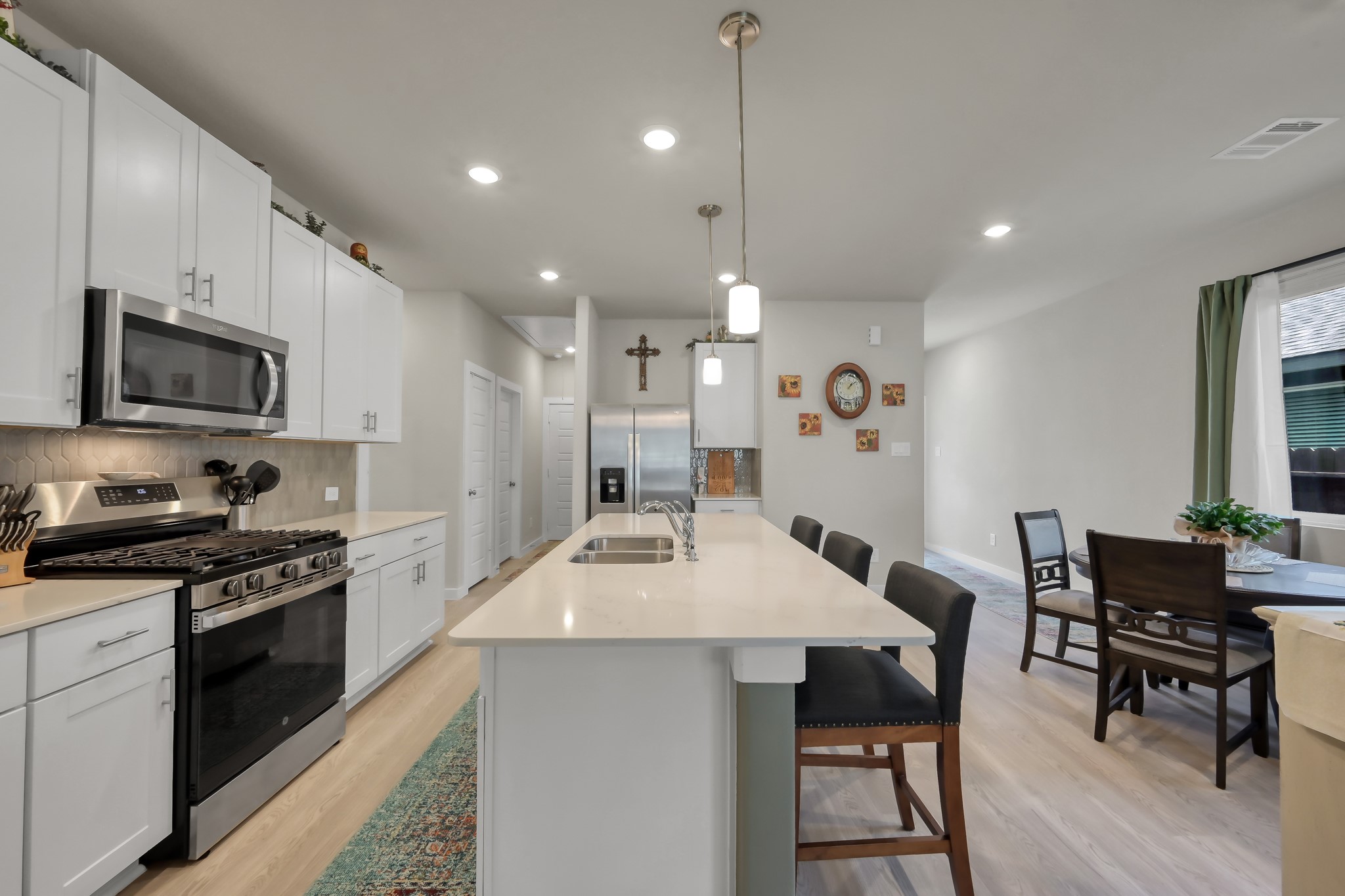 372 Sunrise Rnch Drive Montgomery, TX 77316 - Photo 3 of 32 This modern kitchen features sleek white cabinetry, stainless steel appliances, and a large island with pendant lighting. It seamlessly flows into a bright dining area with large windows, creating an inviting open-concept space.