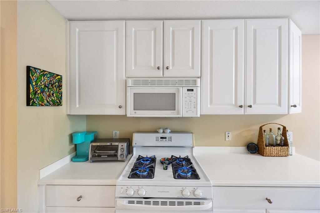 3955 Deer Crossing Court, Unit 103 Naples, FL 34114 - Photo 16 of 40 a kitchen with white cabinets and a stove with wooden floor