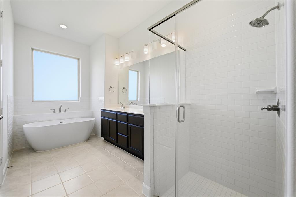 2020 Casting Ridge Mesquite, TX 75181 - Photo 19 of 34 Spa-like bathroom featuring a freestanding tub, glass-enclosed shower with subway tile, a double vanity with dark cabinetry, and light tile flooring