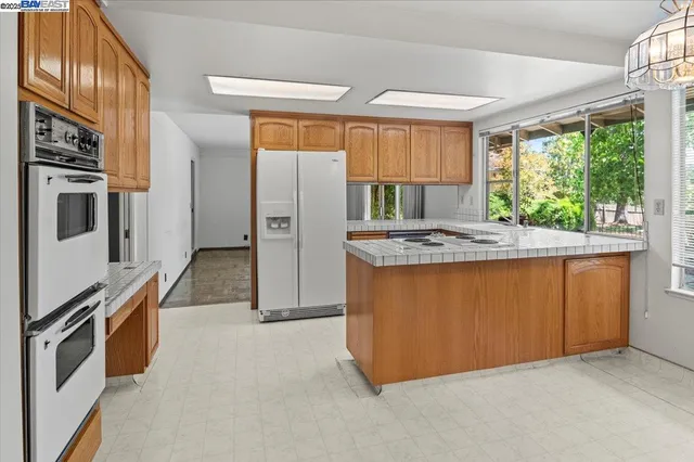 a kitchen with stainless steel appliances granite countertop a refrigerator a sink dishwasher a stove and a dining table with wooden floor