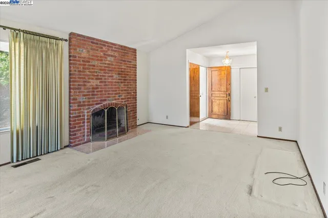 an empty room with windows fireplace and kitchen view