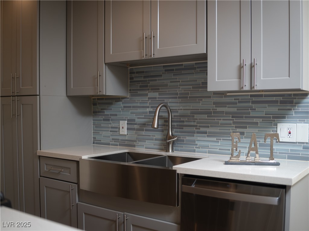 Kitchen featuring gray cabinets, stainless steel dishwasher, tasteful backsplash, and light stone countertops