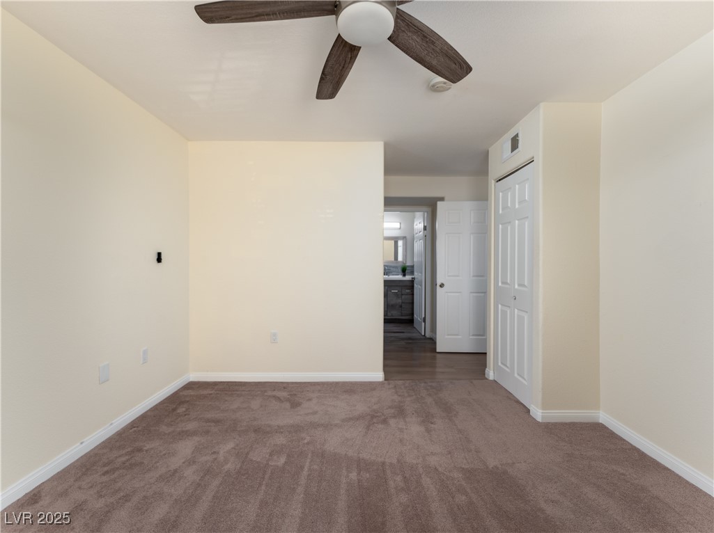 3318 North Decatur Boulevard, Unit 2149 Las Vegas, NV 89130 - Photo 20 of 26 Unfurnished bedroom featuring dark carpet, a closet, ensuite bathroom, and a ceiling fan