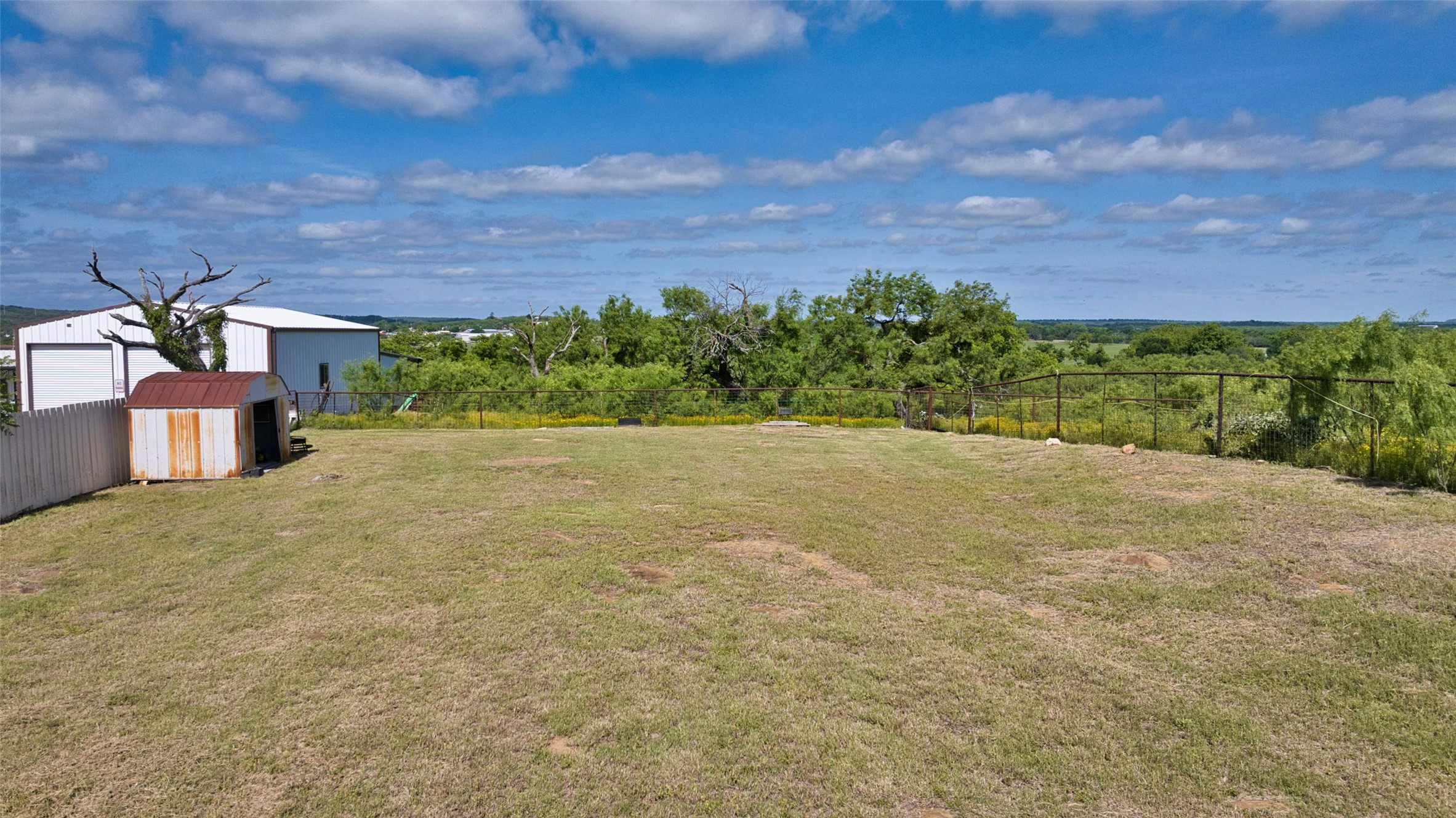 904 Bluebonnet Road Mason, TX 76856 - Photo 9 of 28 Expansive grassy outdoor space featuring a white privacy fence, a metal storage shed, a large white metal outbuilding, and perimeter fencing