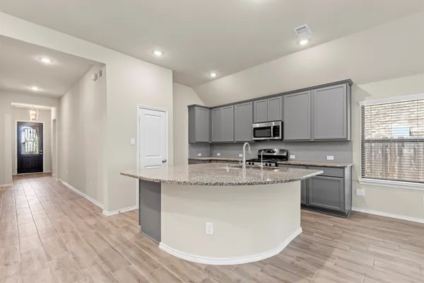 a kitchen with stainless steel appliances granite countertop a stove a sink a refrigerator and white cabinets with wooden floor