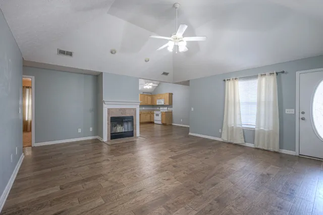 a view of an empty room with wooden floor fireplace and a window