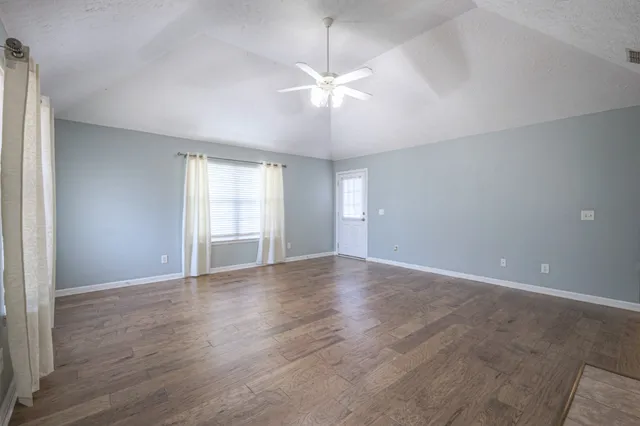a view of an empty room with wooden floor and a window
