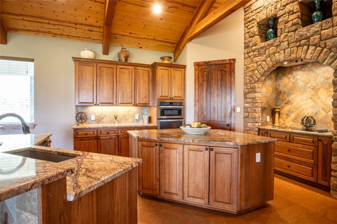 5525 Fm2340 Road Burnet, TX 78611 - Photo 18 of 39 Kitchen with wood ceiling, light stone countertops, brown cabinetry, a center island, and decorative backsplash