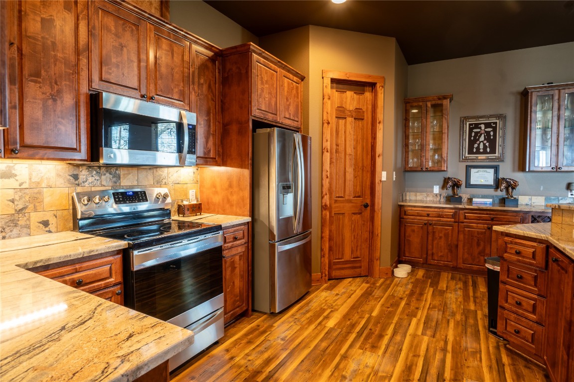 5525 Fm2340 Road Burnet, TX 78611 - Photo 26 of 39 Kitchen featuring appliances with stainless steel finishes, light stone counters, dark wood-style flooring, glass insert cabinets, and brown cabinets