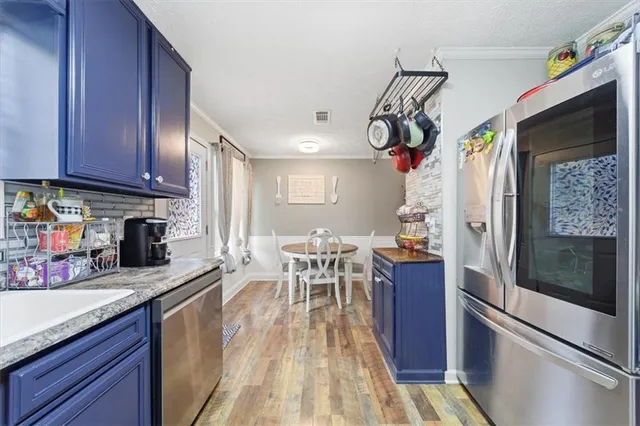 a kitchen with stainless steel appliances granite countertop a refrigerator a sink dishwasher a stove and a dining table with wooden floor