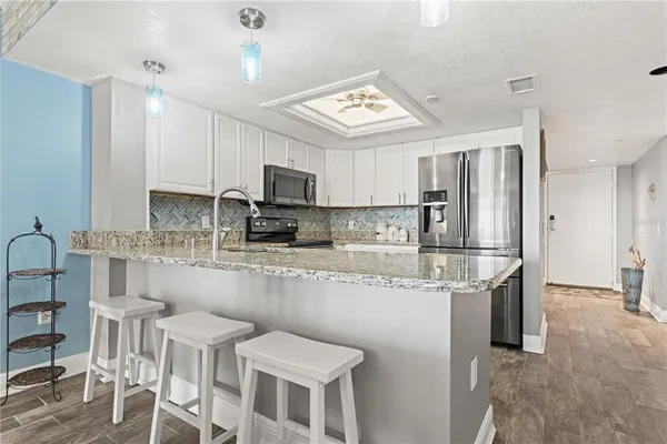 a kitchen with stainless steel appliances granite countertop a sink a stove a refrigerator cabinets and chairs