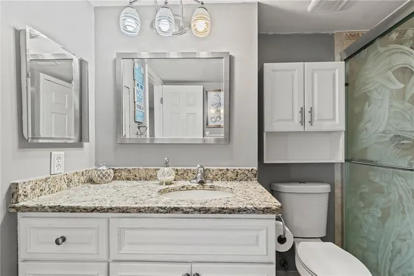 a bathroom with a granite countertop sink a toilet a shower and a mirror