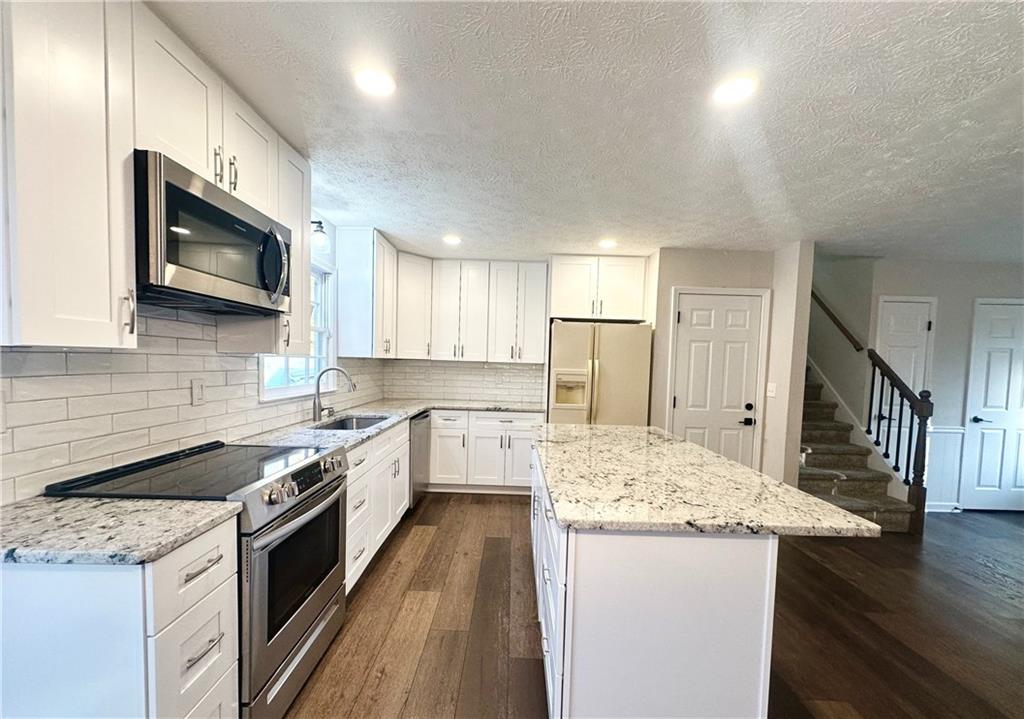 9725 Kings Road Gainesville, GA 30506 - Photo 10 of 32 a kitchen with stainless steel appliances kitchen island granite countertop a stove a sink and a microwave