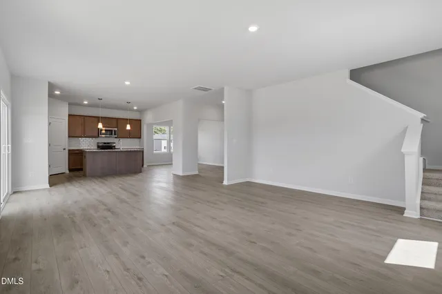 an empty room with wooden floor and kitchen