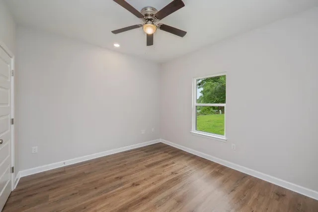 an empty room with wooden floor ceiling fan and windows