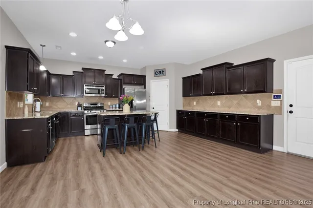 a kitchen with stainless steel appliances kitchen island granite countertop a stove top oven a sink dishwasher a dining table and chairs with wooden floor