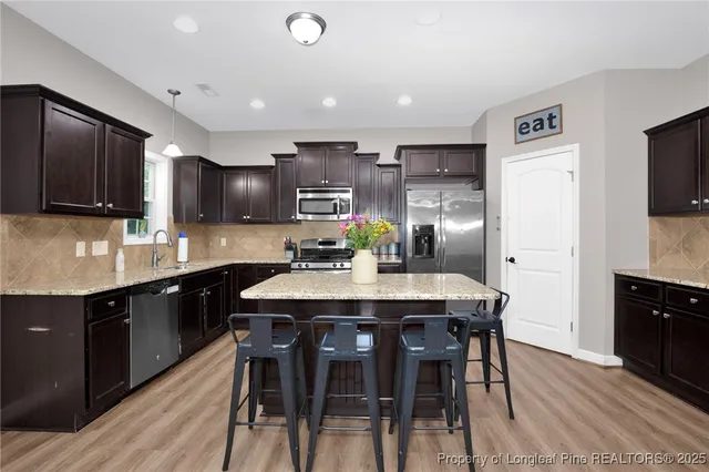 a kitchen with stainless steel appliances kitchen island granite countertop a sink a stove a dining table and chairs