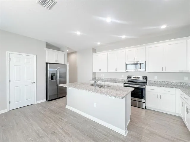 a kitchen with stainless steel appliances granite countertop a stove top oven a refrigerator and white cabinets with wooden floor