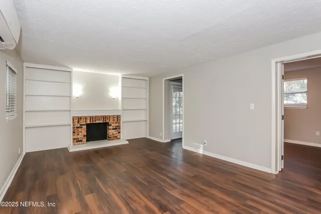an empty room with wooden floor fireplace and windows