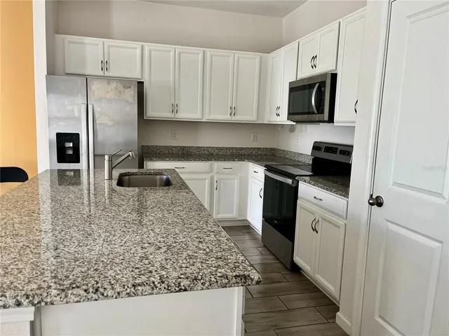 a view of an empty room with chandelier fan and kitchen view