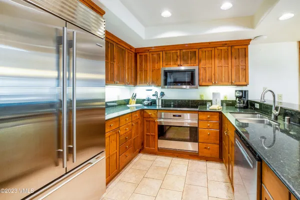 a kitchen with stainless steel appliances granite countertop a refrigerator a stove and a sink with wooden cabinets