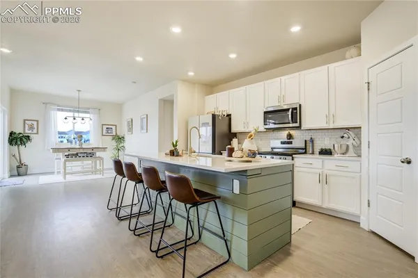 a kitchen with stainless steel appliances granite countertop a sink a stove a refrigerator and white cabinets with wooden floor