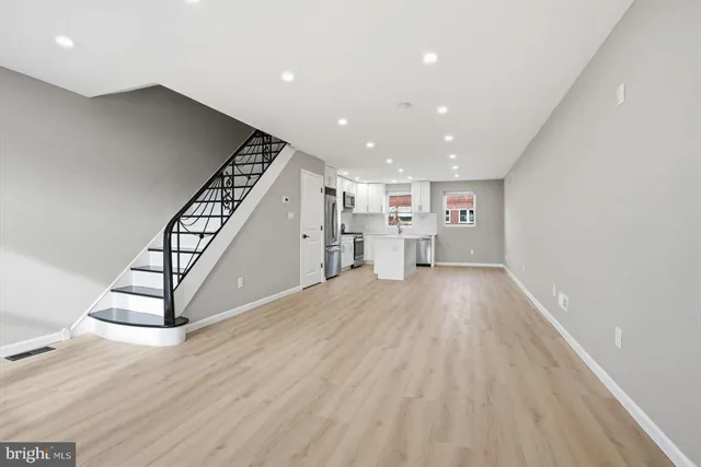 a view of an empty room with wooden floor stairs and a way to kitchen