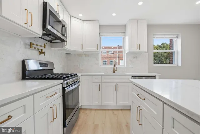 a kitchen with stainless steel appliances granite countertop a sink stove a refrigerator and white cabinets with wooden floor