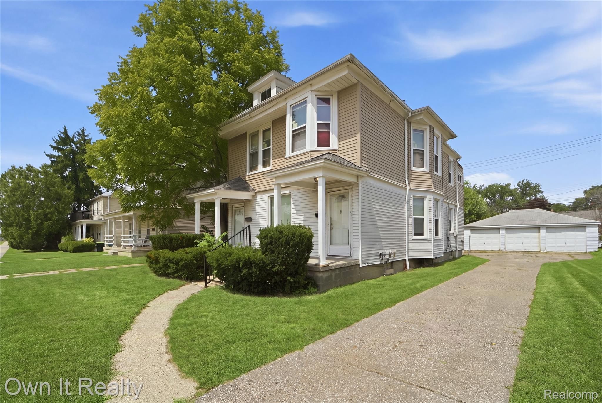 14761 Stephens Road Eastpointe, MI 48021 - Photo 2 of 24 Two-story exterior with light-toned siding, multiple bay windows, covered entryways, a paved driveway, and a detached multi-car garage structure