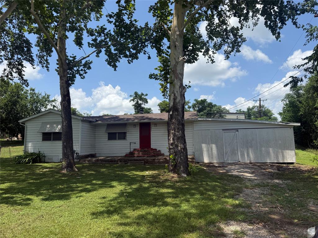 A classic ranch home features a vibrant red entry door and a shaded yard with mature trees.