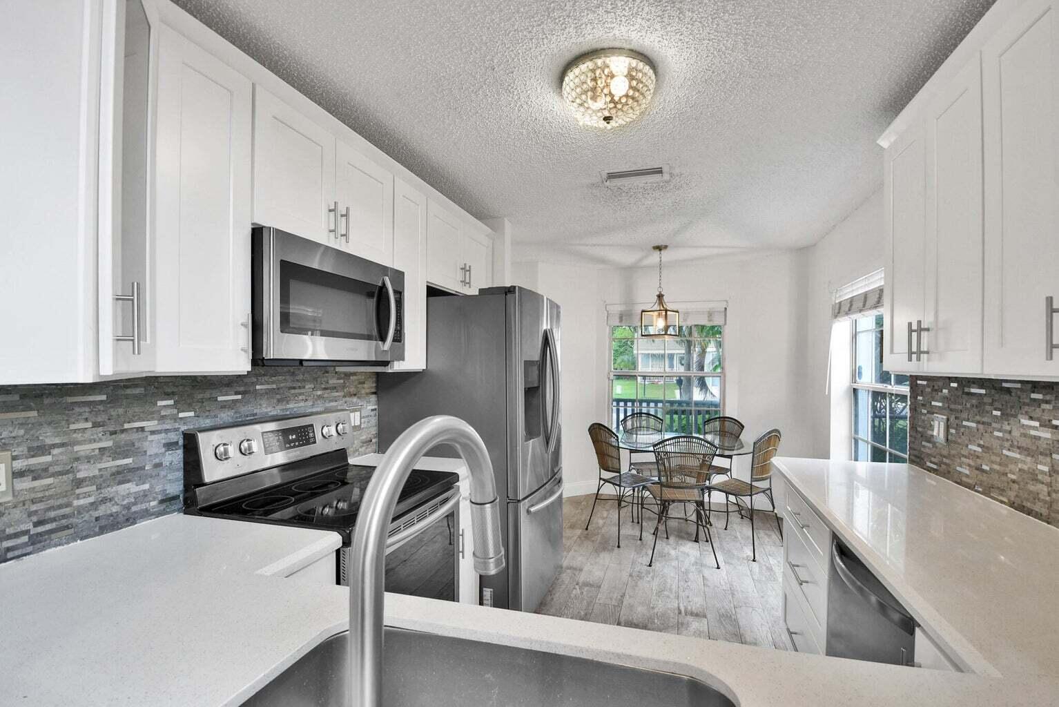 13175 Quiet Woods Road, Unit A Wellington, FL 33414 - Photo 19 of 46 a kitchen with stainless steel appliances granite countertop a stove top oven a sink a dining table and chairs with wooden floor