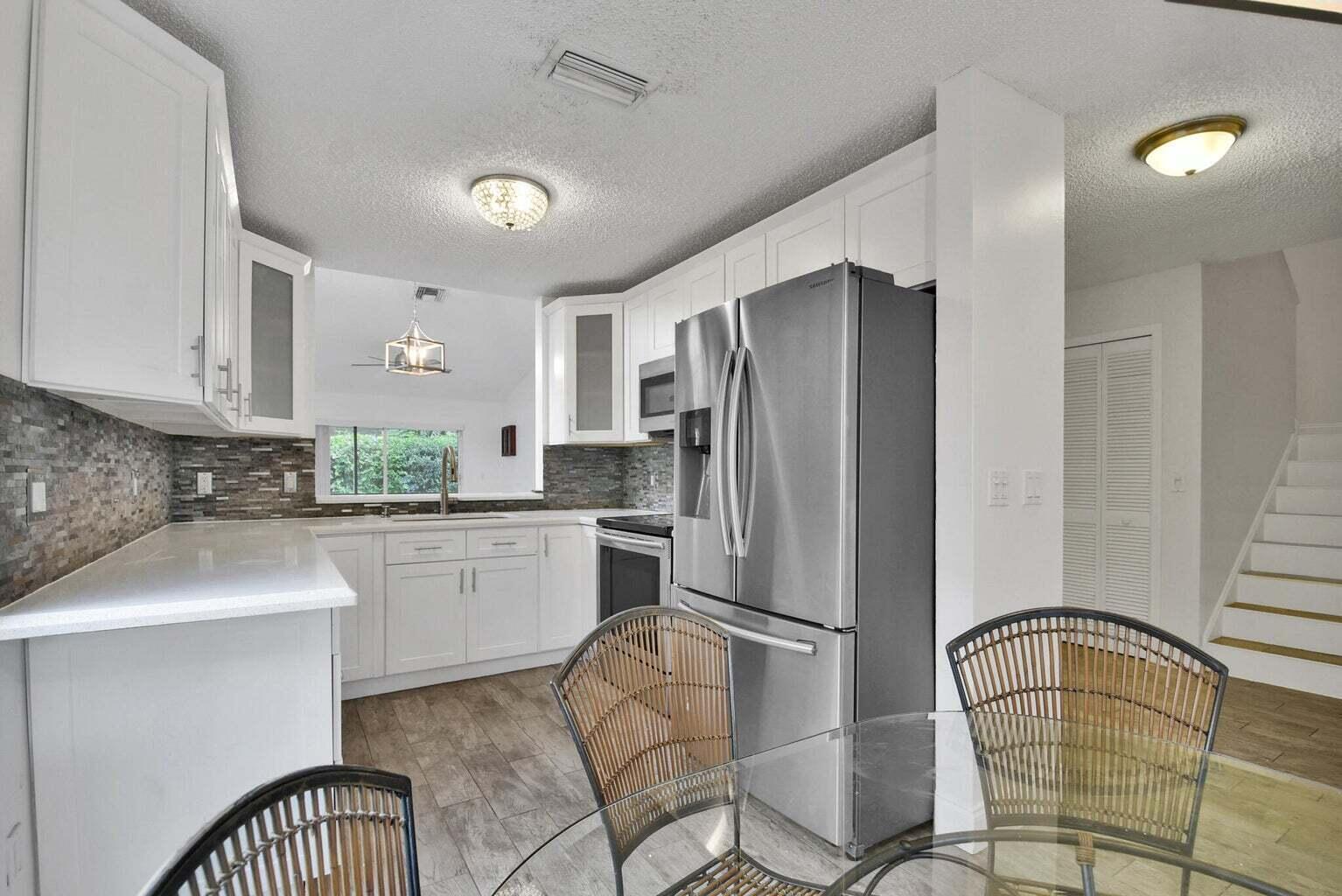 13175 Quiet Woods Road, Unit A Wellington, FL 33414 - Photo 24 of 46 a kitchen with stainless steel appliances granite countertop a refrigerator a sink a stove and white cabinets with wooden floor