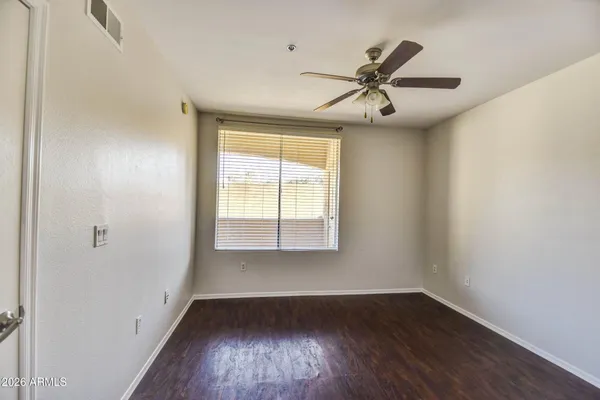 an empty room with wooden floor windows and fan
